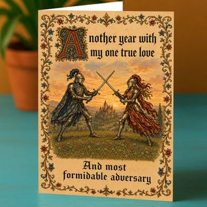 May include: A greeting card featuring an illustration of two knights in armor dueling with swords in a field at sunset. The text reads: Another year with my one true love And most formidable adversary. The card has an ornate floral border.