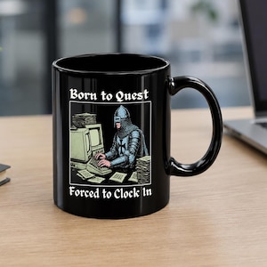 May include: A black ceramic mug featuring a graphic of a knight in armor typing on a vintage computer. The text above the illustration reads Born to Quest and the text below reads Forced to Clock In, both in a white gothic-style font.