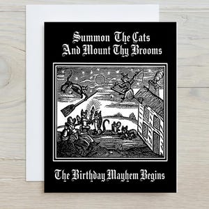 May include: A black and white greeting card featuring a woodcut-style illustration of cats and a witch with the text "Summon The Cats And Mount Thy Brooms" at the top and "The Birthday Mayhem Begins" at the bottom, centred on a white envelope.