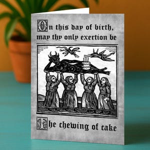 Może przedstawiać: Kartka okolicznościowa z czarno-białą ilustracją. Obraz przedstawia postacie niosące rogatą postać z ciastem. Tekst brzmi: „W dniu urodzin, niech Twoim jedynym wysiłkiem będzie żucie ciasta.”