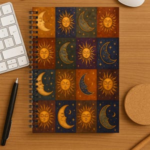 May include: Spiral-bound notebook with a celestial design. The cover features squares with illustrations of the sun and crescent moon in warm colors. The notebook is on a wooden surface with office supplies.