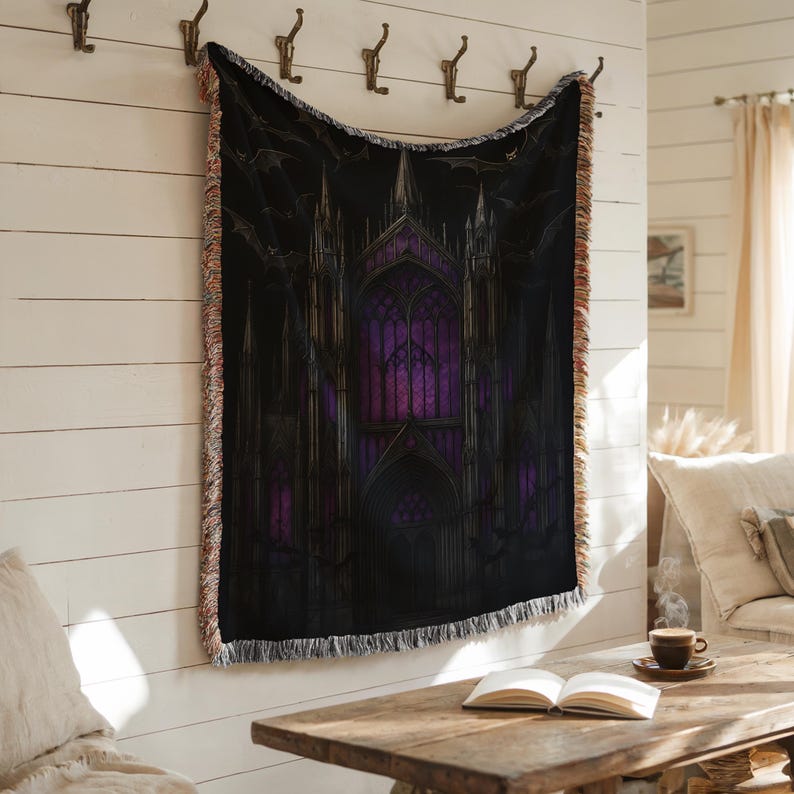 Puede incluir: Una manta negra con un dise&ntilde;o de catedral g&oacute;tica, con vidrieras moradas y murci&eacute;lagos. La manta tiene un borde con flecos y est&aacute; colgada en una pared blanca. El tema es g&oacute;tico y espeluznante.