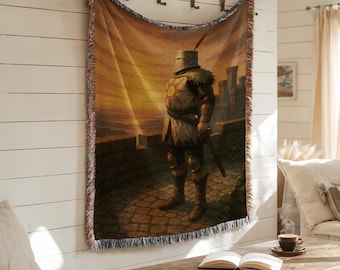 Op de afbeelding: Geweven wandtapijt met een ridder in harnas op een stenen muur, met een zonsondergang op de achtergrond. De ridder heeft een zon-embleem op de borst en een zwaard. Het wandtapijt heeft een franjerand.