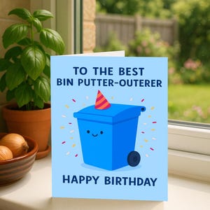 May include: A blue birthday card featuring a cartoon blue bin with a party hat. Text reads "TO THE BEST BIN PUTTER-OUTERER" and "HAPPY BIRTHDAY". The card is set against a window.