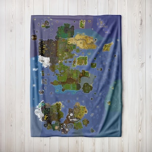 Puede incluir: Una manta rectangular grande con un diseño de mapa detallado. El mapa representa varias masas de tierra, islas y cuerpos de agua en tonos verdes, marrones y azules. La manta se muestra sobre un fondo de tablones de madera de color claro.