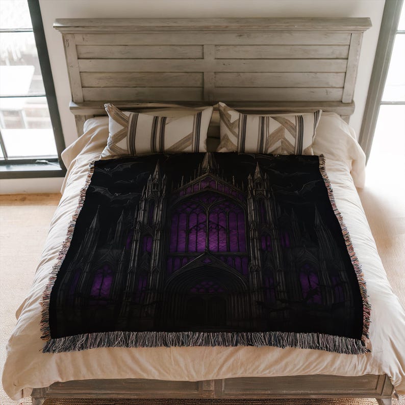 Puede incluir: Una manta negra con un dise&ntilde;o de catedral g&oacute;tica y vidrieras moradas. La manta tiene un borde con flecos y se muestra en una cama con ropa de cama de tonos neutros.