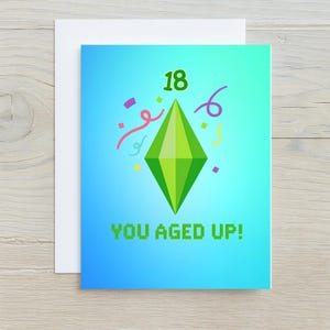 以下が含まれることがあります： 青色のグラデーション背景の誕生日カード。カードには、緑色のひし形、数字の18、緑色のピクセルフォントで「YOU AGED UP！」というテキスト、カラフルな紙吹雪が描かれています。