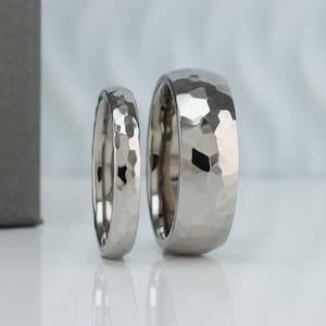 May include: Two silver-toned metal rings with a hammered, faceted texture. The rings feature a reflective, polished finish with irregular indentations across the outer surface, creating a multi-faceted appearance that catches light from various angles.