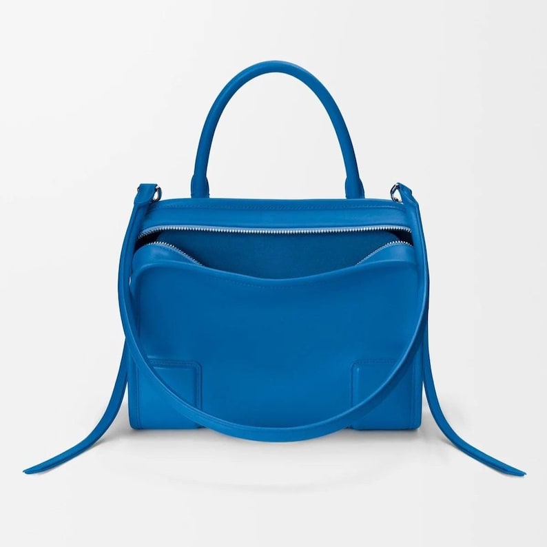Pode incluir: Uma mala azul brilhante com uma al&ccedil;a superior e uma al&ccedil;a de ombro remov&iacute;vel. A mala tem formato retangular com abertura superior com z&iacute;per. O interior &eacute; azul combinando. A mala &eacute; feita de material liso.
