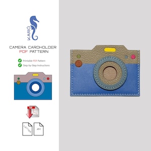 Op de afbeelding: Een blauw en bruin lederen camera kaarthouder met een cirkelvormig lensontwerp. De kaarthouder heeft een blauwe basis en een bruine bovenkant, met gele en roze accenten. De tekst "CAMERA CARDHOLDER PDF PATTERN" is zichtbaar.