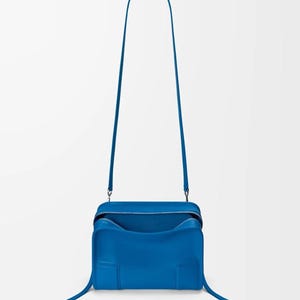 Pode incluir: Uma vibrante bolsa transversal azul com formato retangular e uma al&ccedil;a longa e fina. A bolsa possui fecho de z&iacute;per e um interior espa&ccedil;oso. O design &eacute; moderno e minimalista, com linhas limpas e uma cor s&oacute;lida.