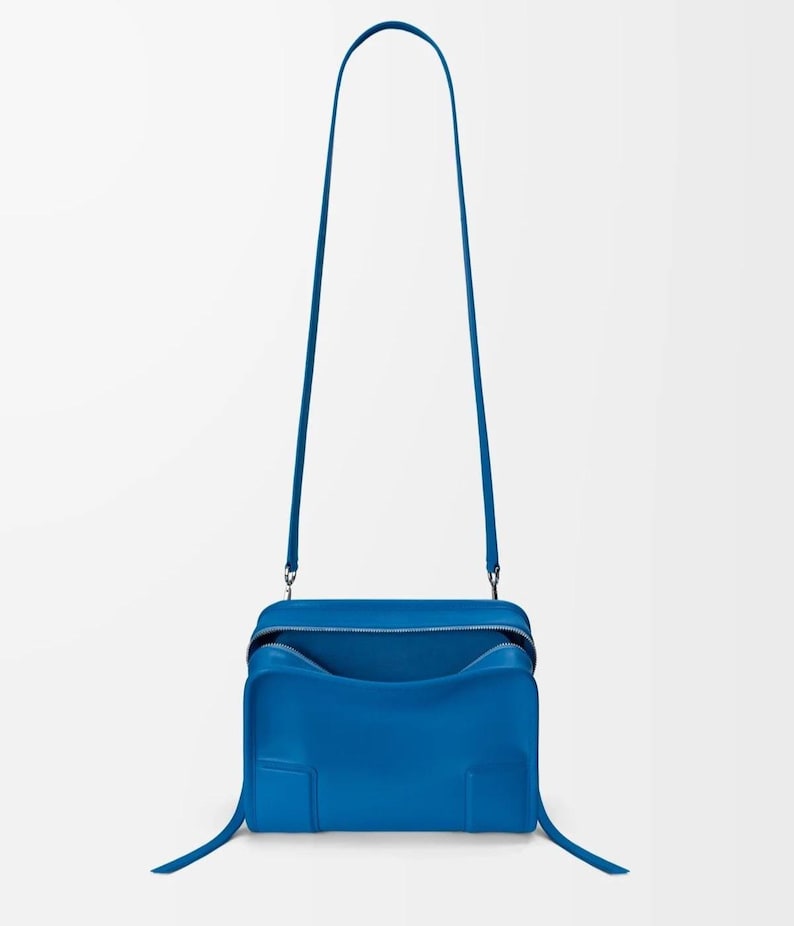 Pode incluir: Uma vibrante bolsa transversal azul com formato retangular e uma al&ccedil;a longa e fina. A bolsa possui fecho de z&iacute;per e um interior espa&ccedil;oso. O design &eacute; moderno e minimalista, com linhas limpas e uma cor s&oacute;lida.
