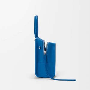 Pode incluir: Uma mala azul brilhante com formato retangular e uma al&ccedil;a superior. A mala apresenta um z&iacute;per prateado parcialmente aberto, revelando o interior. Uma al&ccedil;a longa e fina se estende da parte inferior da mala. A mala est&aacute; sobre um fundo branco.