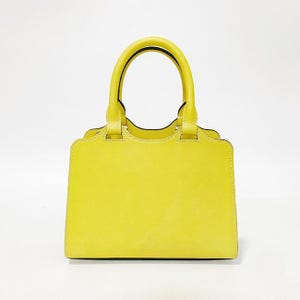 May include: A bright yellow handbag with a structured rectangular body, two rounded top handles, and visible white stitching along the edges. The bag features a scalloped top silhouette and a smooth, matte finish, presenting a clean and simple design.
