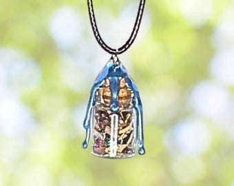 May include: A pendant necklace featuring a clear, rectangular resin pendant with a blue, dripped-paint design. The pendant contains small, colorful objects. The necklace has a black cord.