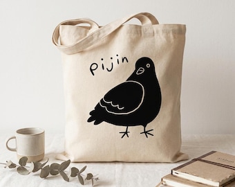 May include: A beige canvas tote bag featuring a black graphic illustration of a pigeon and the text "pijin" printed in black. The bag has two top handles and a rectangular shape, showcasing a simple line-art style design on the front.
