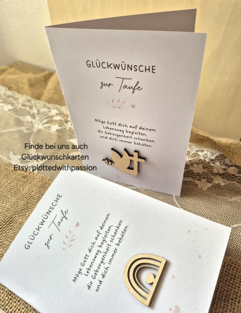 May include: Two white greeting cards for a baptism, each featuring German text and a wooden cutout. One card displays a dove and cross, while the other features a rainbow with a heart. The cards include the printed text GL&Uuml;CKW&Uuml;NSCHE zur Taufe.