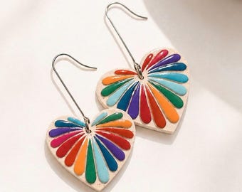 Puede incluir: Un par de pendientes en forma de corazón con un diseño de abanico arcoíris. Los pendientes tienen una base de color crema con rayas coloridas en rojo, naranja, amarillo, verde, azul y morado. Los pendientes tienen ganchos plateados.