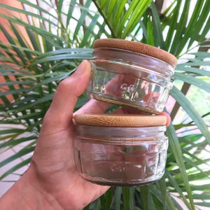 May include: Two clear glass jars with bamboo lids. The jars are stacked on top of each other. The jars have a textured surface and are empty.
