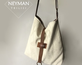 May include: A white canvas tote bag with a brown strap and a brown leather tag that says "NEYMAN TBILISI".