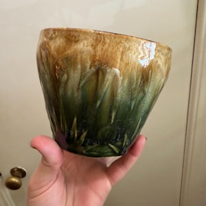 May include: A ceramic bowl with a unique glaze. The top of the bowl is a warm brown, transitioning to a deep green at the base. The glaze has a textured, organic appearance, giving the bowl a handcrafted feel.