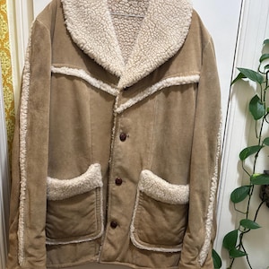 May include: A brown suede jacket with a white faux fur collar and lining. The jacket has two large pockets with white faux fur trim and a button closure.