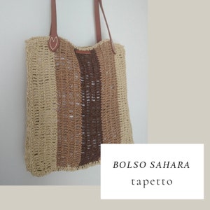 Könnte beinhalten: Eine braune, beige und cremefarbene gestreifte gehäkelte Tragetasche mit Ledergriffen. Die Tasche hat ein herzförmiges Detail auf der Vorderseite und der Text "BOLSO SAHARA tapetto" ist in der rechten unteren Ecke sichtbar.