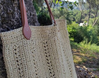 May include: A beige crocheted tote bag with brown leather straps. The bag has a simple, classic design and is ideal for carrying everyday essentials.