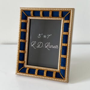 May include: A rectangular photo frame with a gold-colored border and navy blue velvet accents. The frame is 5" x 7" and features the text "L.D. Larets". The frame has a decorative gold beaded trim.