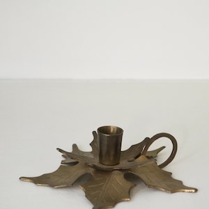 Puede incluir: Un candelero de metal dorado con forma de hoja y una abertura redonda para una vela.