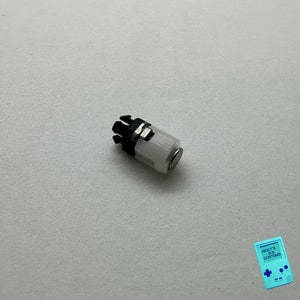 May include: A small, white, cylindrical object with a black plastic cap and a silver metal clip. The object has a small, round magnet on one end.