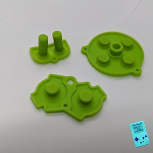 May include: A set of four green replacement buttons for a video game controller. The buttons are made of soft silicone and have a raised, circular shape.