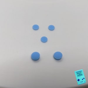 Peut inclure: Cinq boutons ronds bleu clair sur une surface blanche.