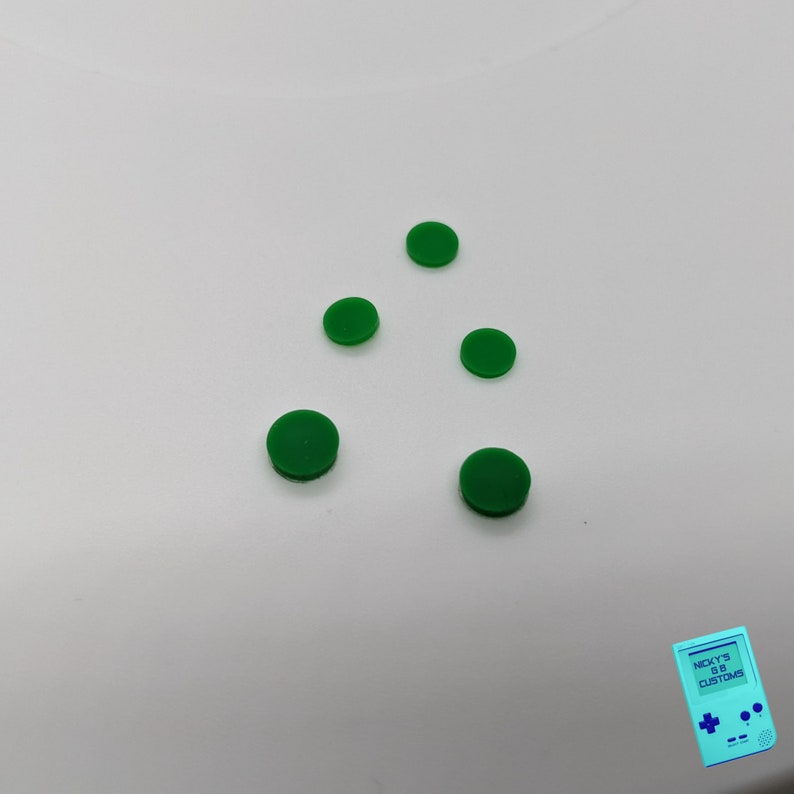 Peut inclure: Cinq boutons ronds verts sur une surface blanche.