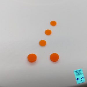 Peut inclure: Cinq boutons ronds orange sur un fond blanc. Les boutons sont dispos&eacute;s en un motif, avec deux boutons en bas, deux boutons au milieu et un bouton en haut.