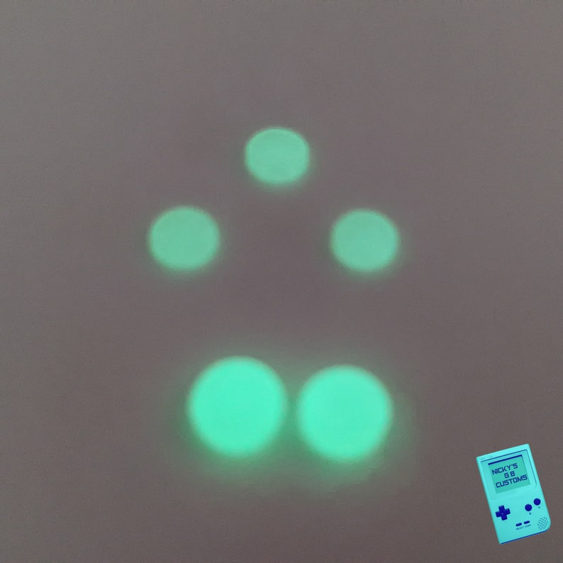 Peut inclure: Cinq cercles verts brillants dispos&eacute;s en forme de triangle avec deux cercles en bas. Les cercles sont sur un fond gris clair. Un petit appareil de style Game Boy bleu et blanc avec le texte "NICKY'S G18 CUSTOMS" se trouve dans le coin inf&eacute;rieur droit.