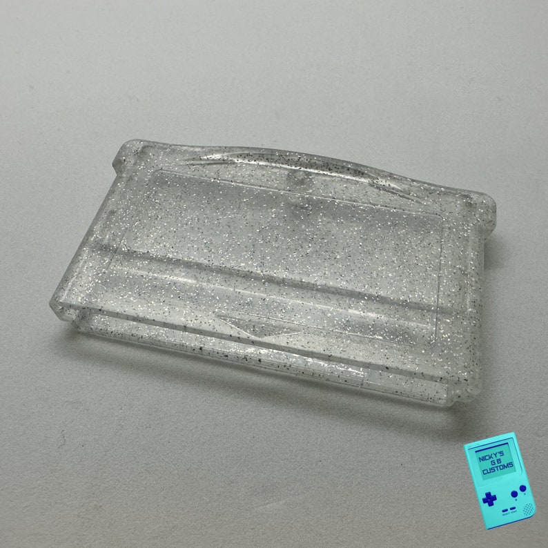 May include: A clear plastic Game Boy Color game cartridge case with a silver glitter finish.