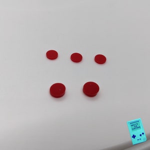 Peut inclure: Cinq boutons ronds rouges sur une surface blanche.