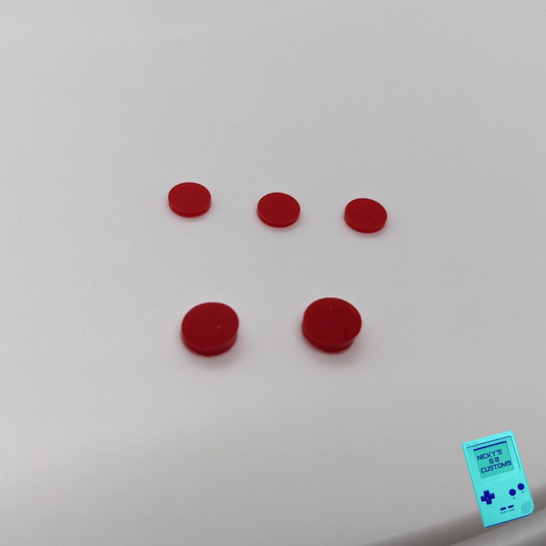 Peut inclure: Cinq boutons ronds rouges sur une surface blanche.