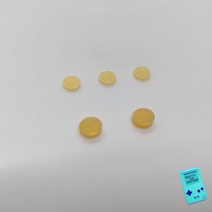 Peut inclure: Cinq petits boutons en caoutchouc ronds, translucides et jaune clair.