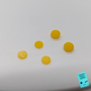 Peut inclure: Cinq boutons ronds jaunes sur une surface blanche.
