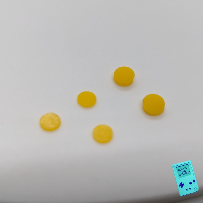 Peut inclure: Cinq boutons ronds jaunes sur une surface blanche.