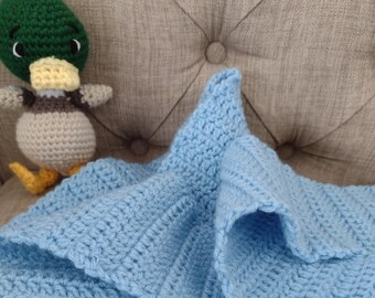 Puede incluir: Una manta de bebé de crochet azul claro con un juguete de crochet de pato en una superficie marrón texturizada.