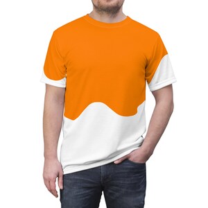 Puede incluir: Una camiseta de manga corta y cuello redondo con un diseño bicolor que presenta una sección superior de color naranja brillante y una sección inferior blanca, separadas por una línea ondulada horizontal que cruza la prenda.