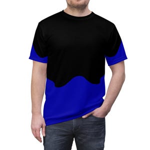 Peut inclure: Un t-shirt à manches courtes et col rond présentant un design bicolore. La partie supérieure du t-shirt est noir uni, tandis que la partie inférieure est d'un bleu roi vif. Les deux couleurs se rejoignent par une ligne horizontale ondulée.