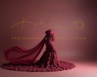 May include: A pregnant person wearing a long, flowing, burgundy dress made entirely of flowers. The dress has a sheer, burgundy cape that is flowing in the wind. The background is a solid burgundy color.
