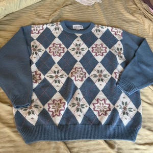 May include: A blue sweater with a white and brown diamond pattern. The sweater has a crew neck and long sleeves. The label on the sweater reads "Alfred Dunner".