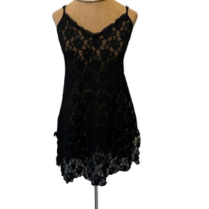 May include: Black lace slip dress with spaghetti straps and a scalloped neckline. The dress features a floral lace pattern and a ruffled hem. The garment is displayed on a mannequin.