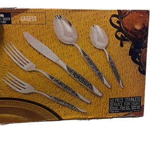 May include: A silver 50-piece stainless steel flatware set for eight, displayed on a cardboard box. The set includes forks, knives, and spoons with decorative handles. The box is labeled "CARESS".
