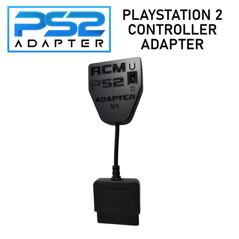 May include: Black PlayStation 2 controller adapter. The adapter has the text "PS2 ADAPTER" in blue and white. The adapter also has the text "RCMU PS2 D ADAPTER VE" in black.